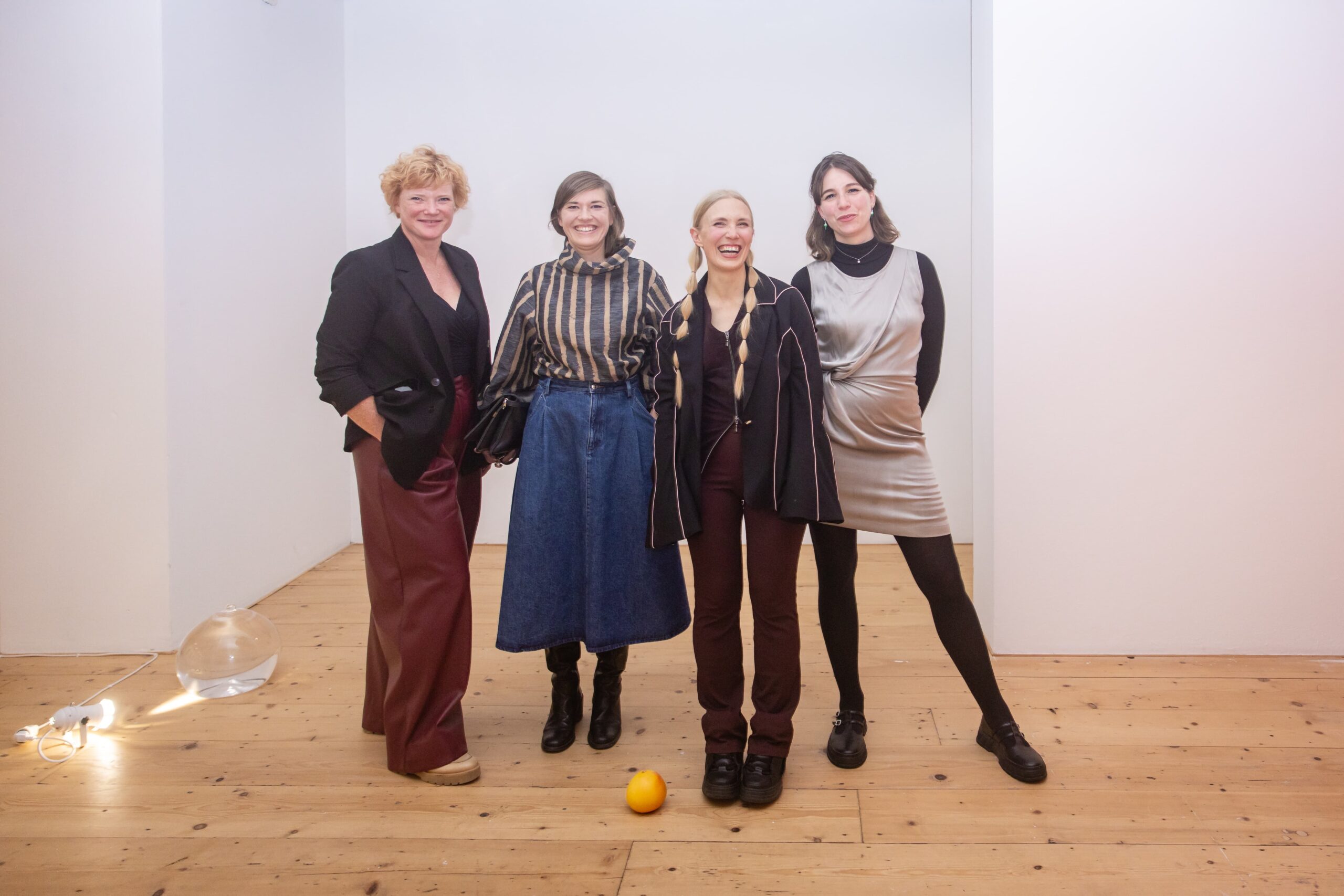 Four women stand side by side in an exhibition space. They are looking directly at the camera and smiling.