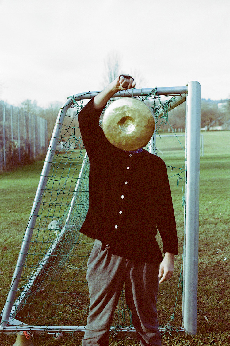 A man stand in a field, the is a goal post behind him. He holds a golden gong in front of his face.