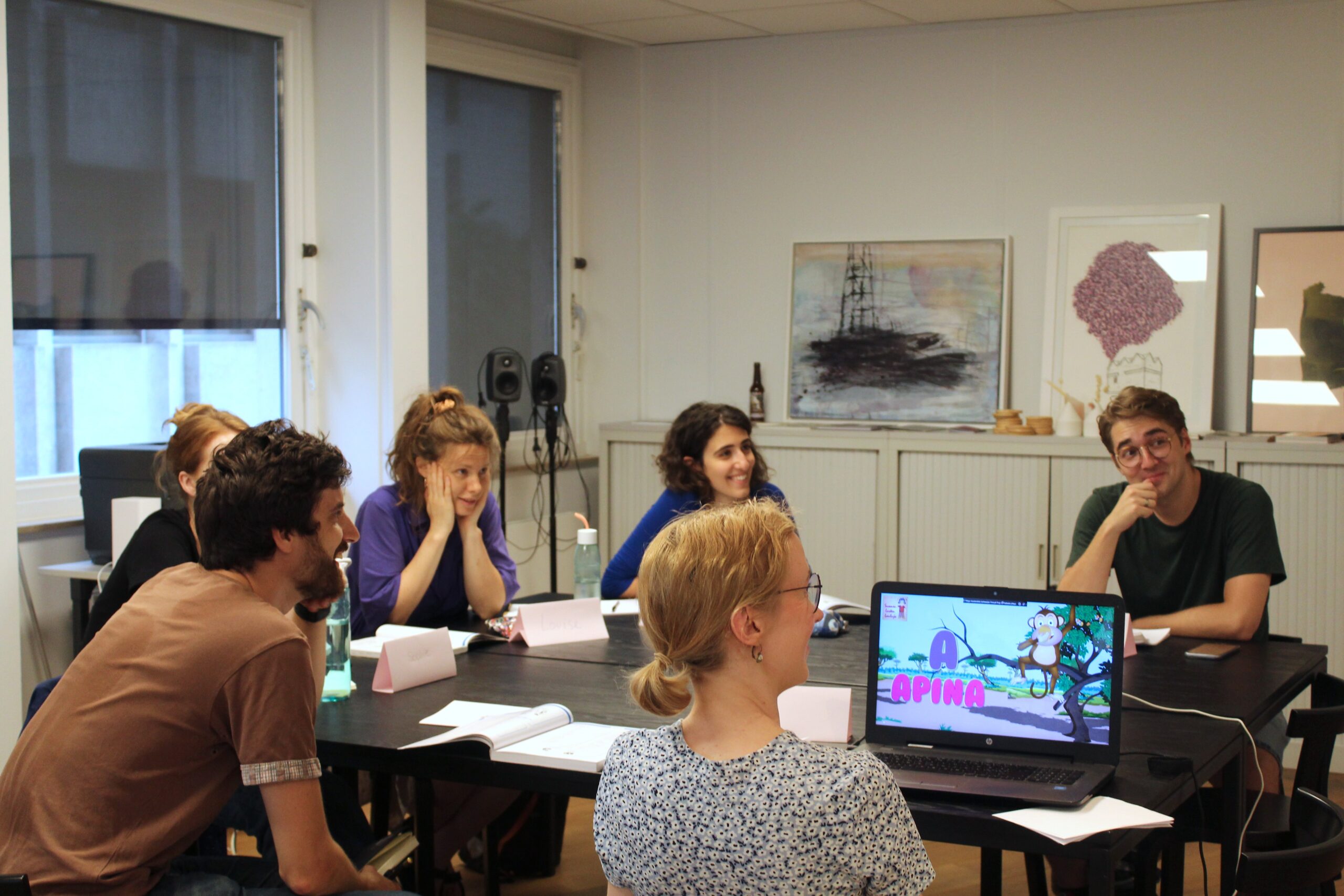 Students and teacher sit around a table at the Institute office. There is a laptop open infront of the picture and the students are looking up at a projector that is out of the image.