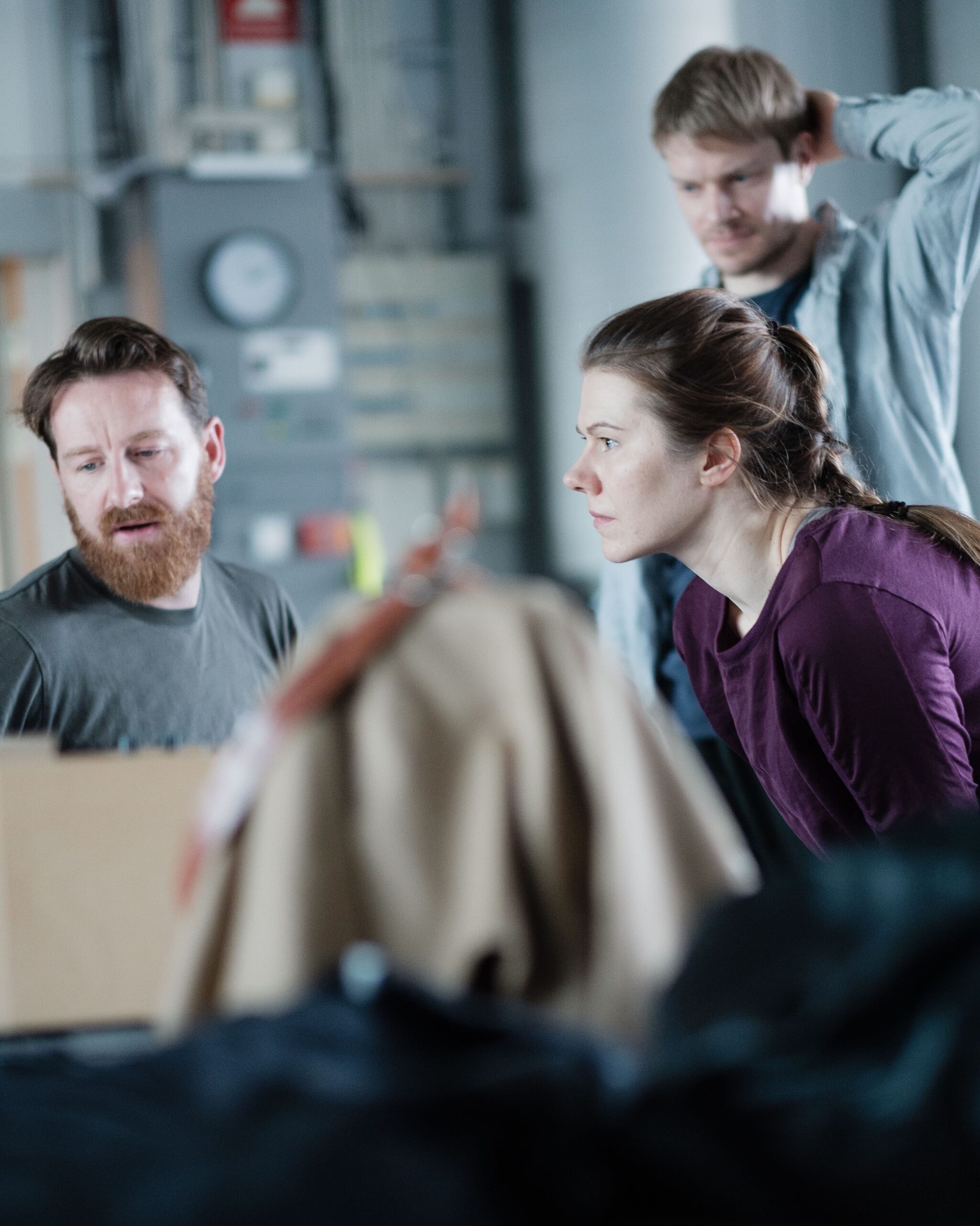 Two men and a woman are looking at something out of shot, possible an image or a screen.. They appear to be in discussion. They are wearing relaxed clothing. The foreground and background are out of focus.