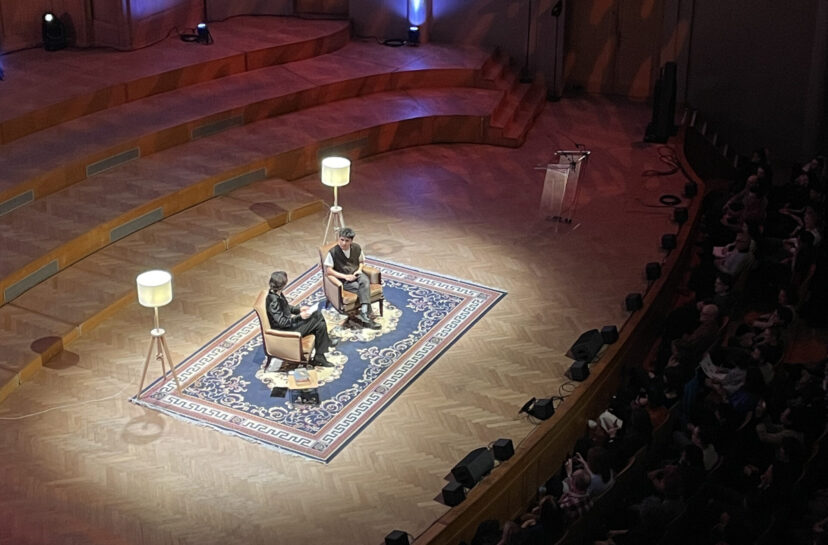 Ocean Vuong’s talk (March 2026) at BOZAR. Photo by Tilda Forss. Two men are seated on a. stage in armchairs, situated on a large rug and flanked by two standing lamps. The atmosphere recreates a living room atmosphere on a stage.