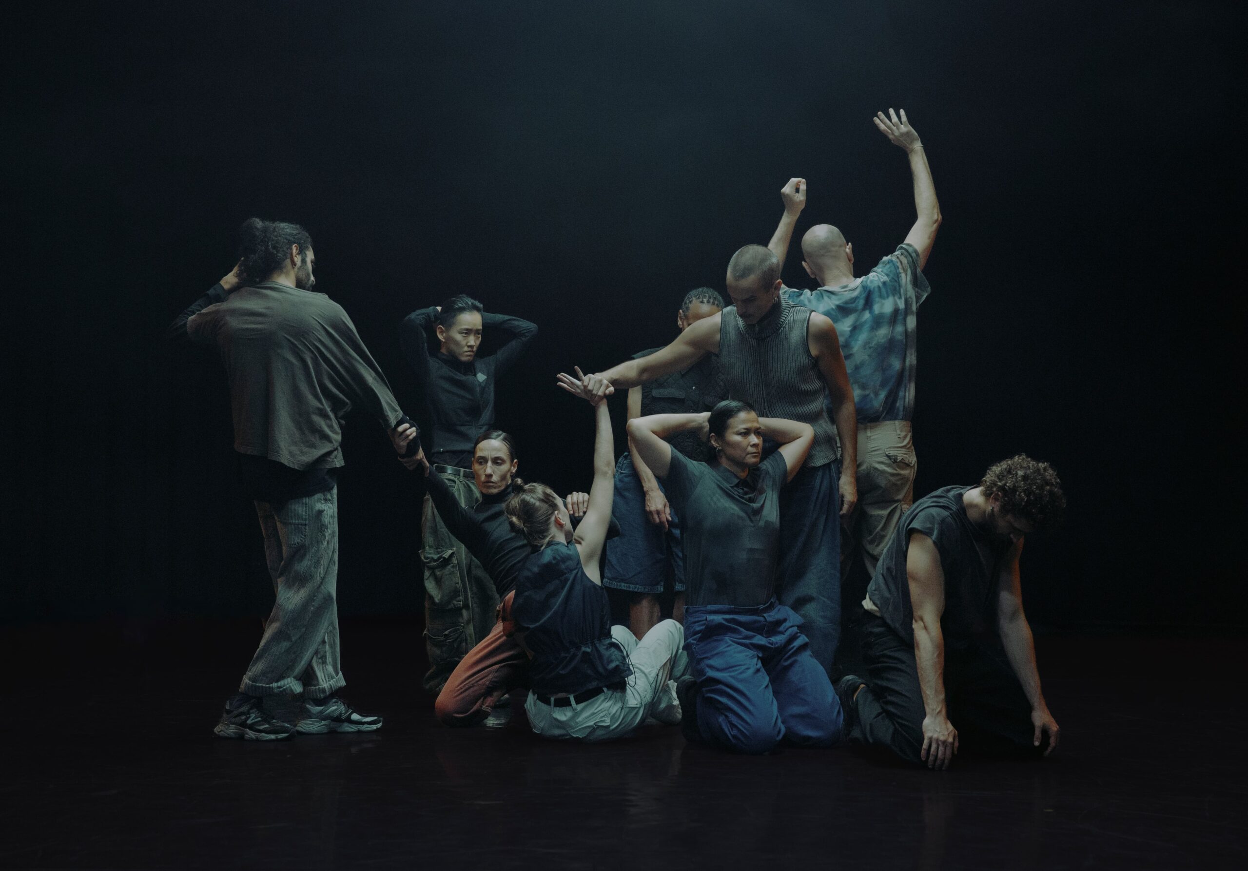 Nine dancers on stage. They are positioned against a black background.