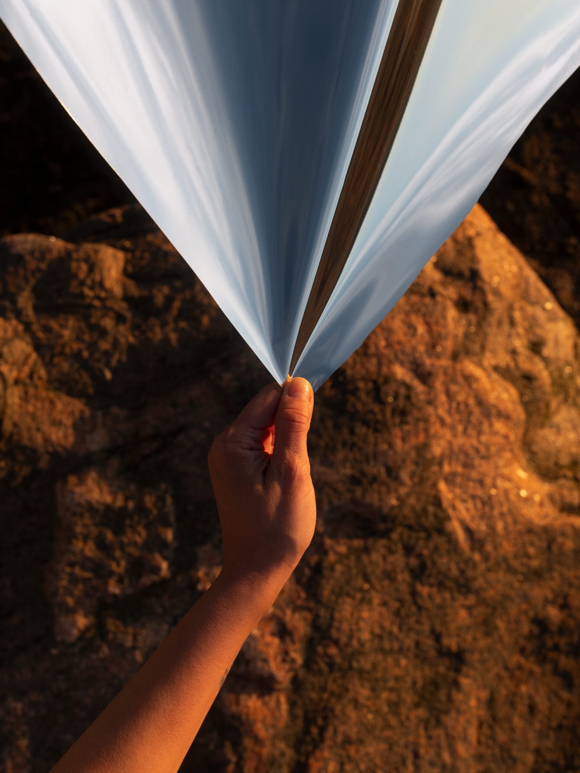 A hand pulls down on a a light blue coloured textile. In the background is a cave like brick wall, lit up by a warm light.