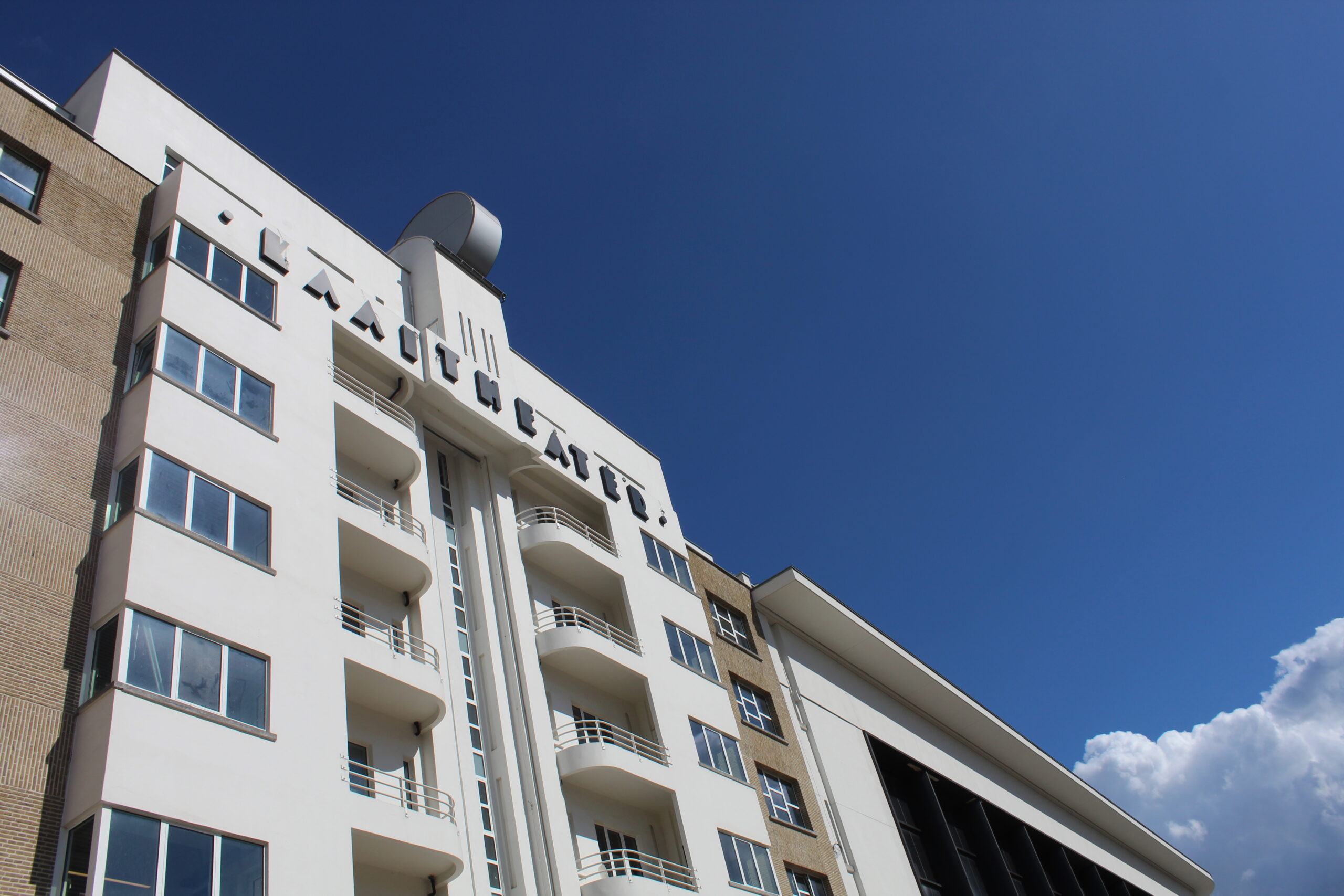 A white building with the words KAAITHEATER at the top. A bight blue sky behind.